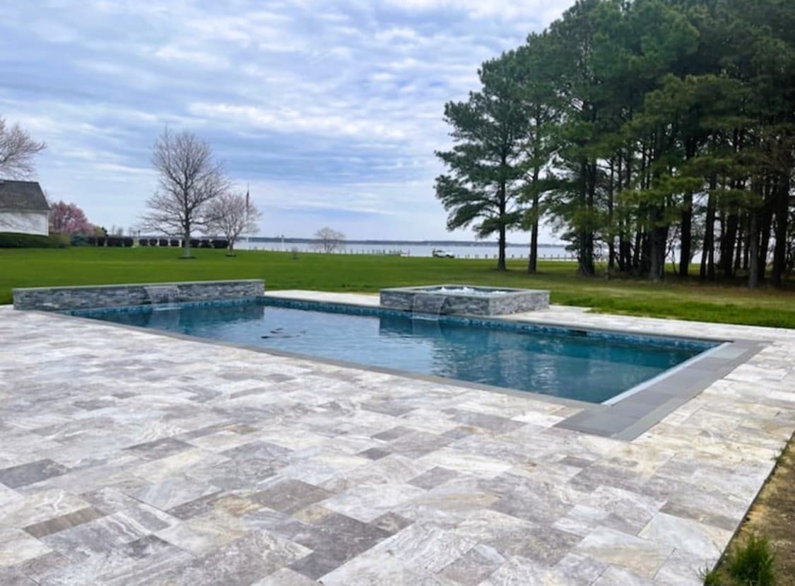 Classic rectangular pool with raised spa and travertine decking on a waterfront property.