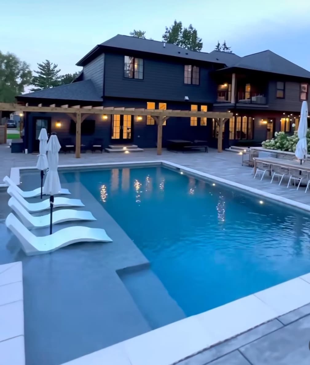 Modern pool with in-water tanning ledge loungers and pergola at dusk.