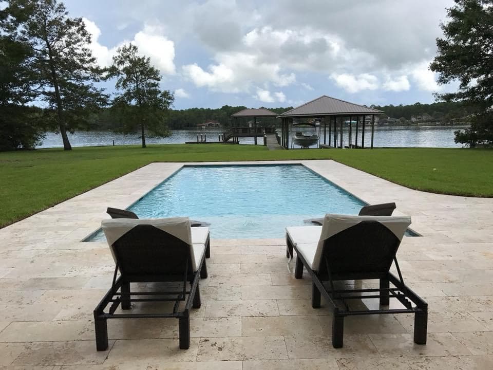 Rectangular pool with travertine decking on a waterfront property.