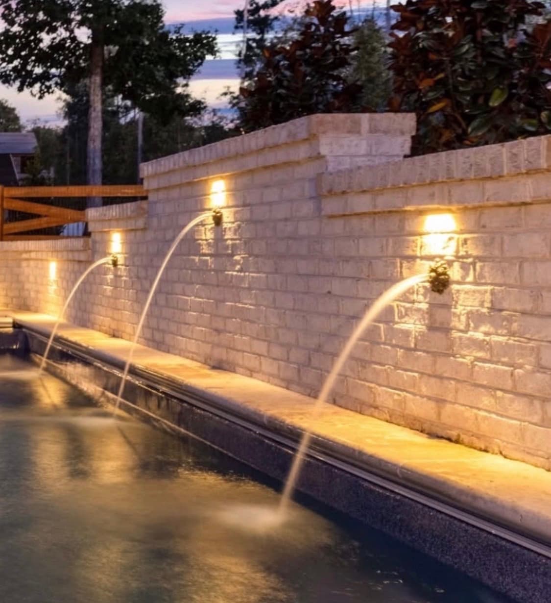 Sheer descent water features with evening lighting flowing into a custom pool.