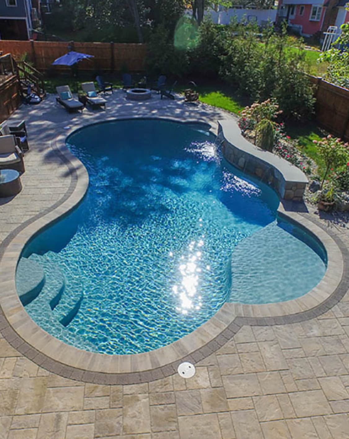 Freeform pool design with paver decking and natural curves viewed from above.