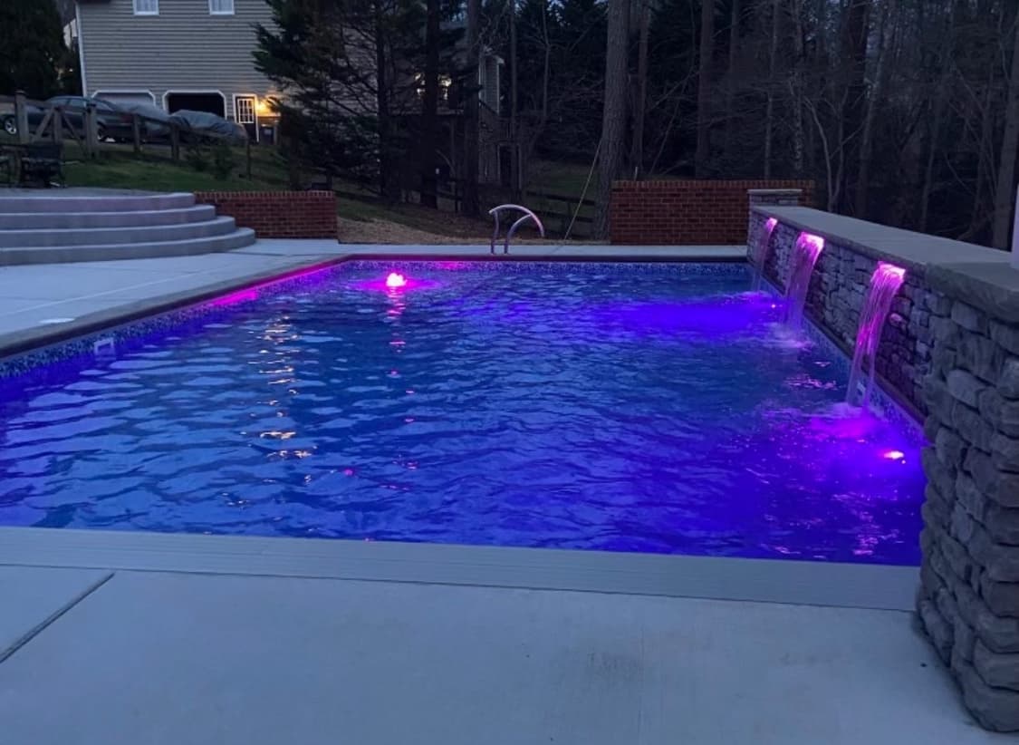 Custom pool illuminated with vibrant LED lighting and sheer descents at night.