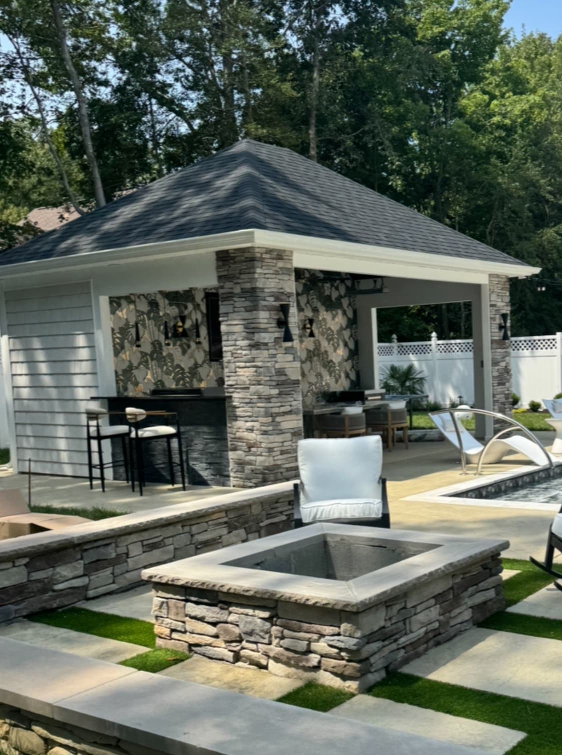 Stone fire pit with pool house and seating area beside a custom pool.